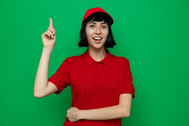 Surprised young caucasian delivery woman pointing up looking 