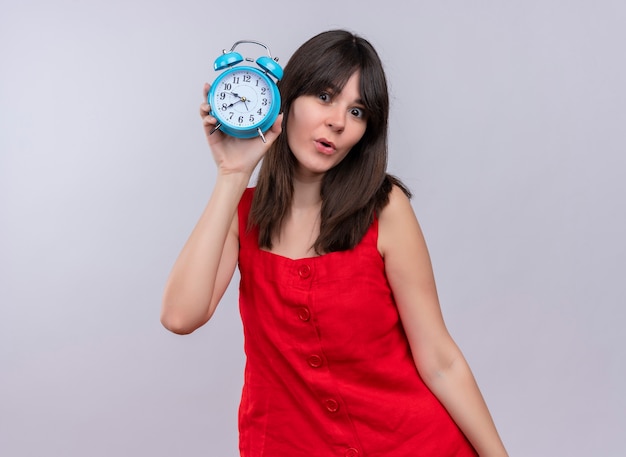 Surprised young caucasian girl holding clock and looking at camera on isolated white background 0