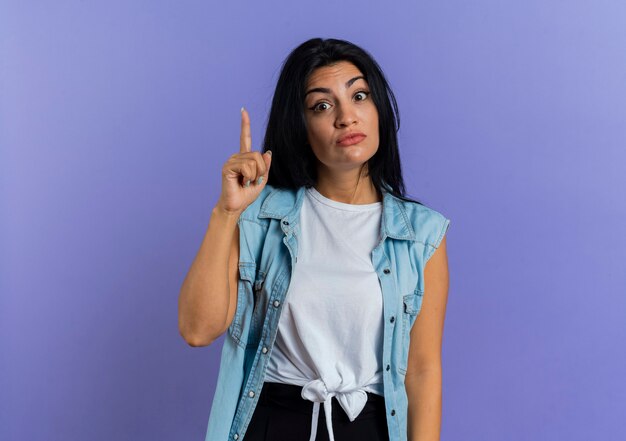 Surprised young caucasian girl points up isolated on purple background with copy space