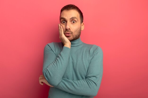 Surprised young caucasian man  putting hand on face isolated on crimson wall with copy space