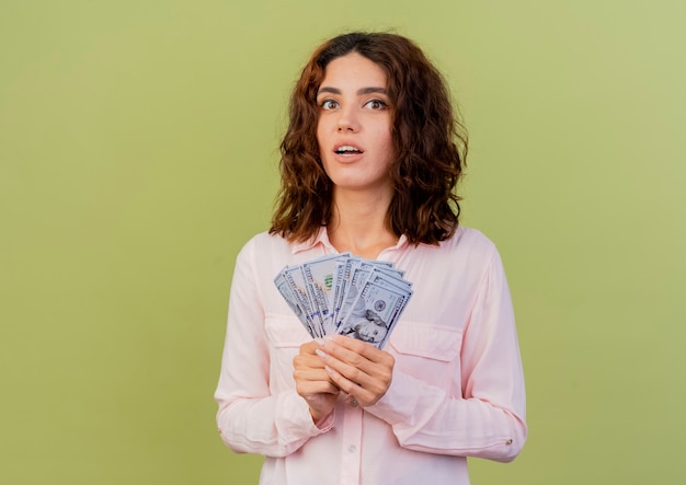 Surprised young caucasian woman holds money isolated on green background with copy space