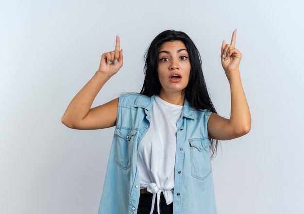 Surprised young caucasian woman points up with two hands