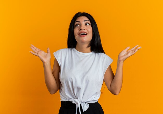 Surprised young caucasian woman stands with raised hands looking at side