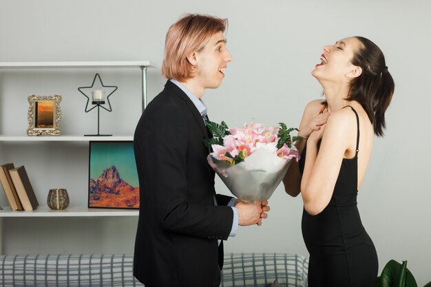 놀란 젊은 부부는 발렌타인 데이에 거실에 서 있는 꽃다발 소녀 속삭임으로 서로를 껴안았다