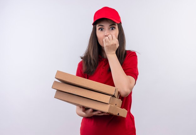 孤立した白い壁にピザの箱を保持している赤い帽子に赤いtシャツを着て驚いたの若い配達の女性