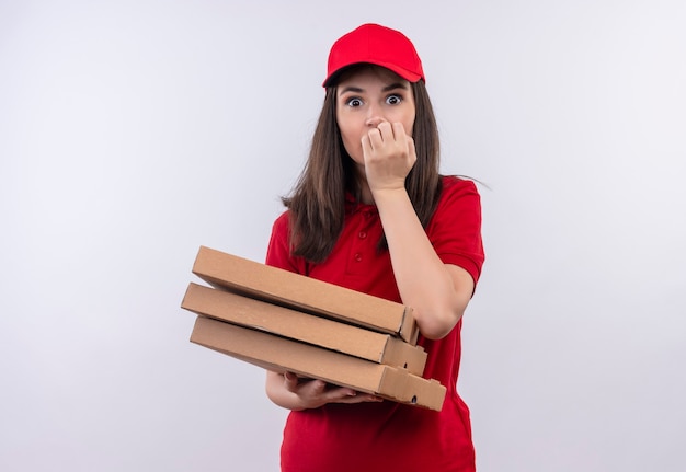 Surprised young delivery woman wearing red t-shirt in red cap holding a pizza box on isolated white wall
