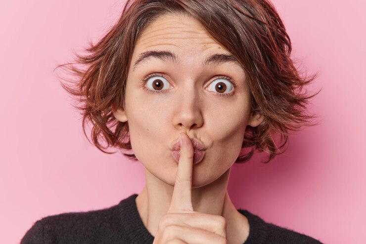 Free Photo surprised young european woman stares bugged eyes makes silence gesture spreads rumors has trendy hairstyle tells secret isolated over pink studio background. body language and shushing concept