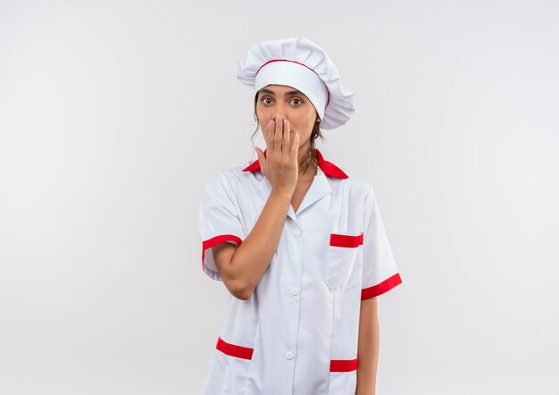 Удивленная молодая женщина-повар в униформе шеф-повара закрыла рот рукой с копией пространства