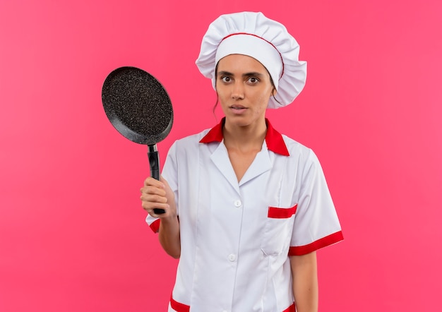 Surprised young female cook wearing chef uniform holding frying pan with copy space