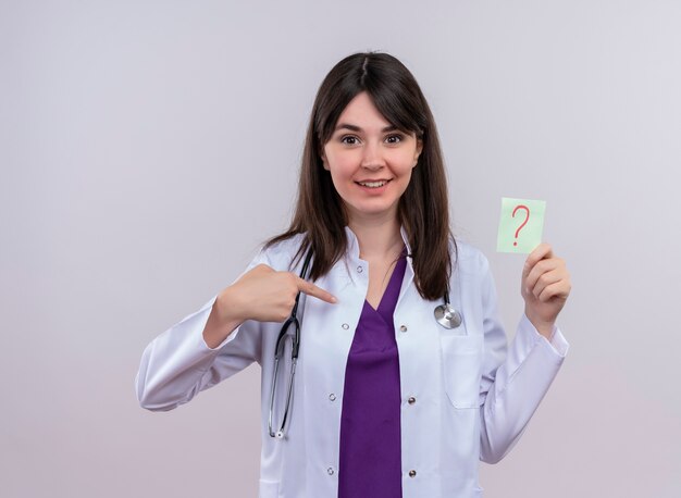 Удивленная молодая женщина-врач в медицинском халате со стетоскопом указывает на себя и держит вопросительный знак на изолированном белом фоне с копией пространства