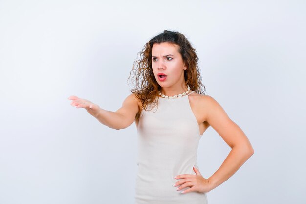 Surprised young girl is extending hand to right on white background