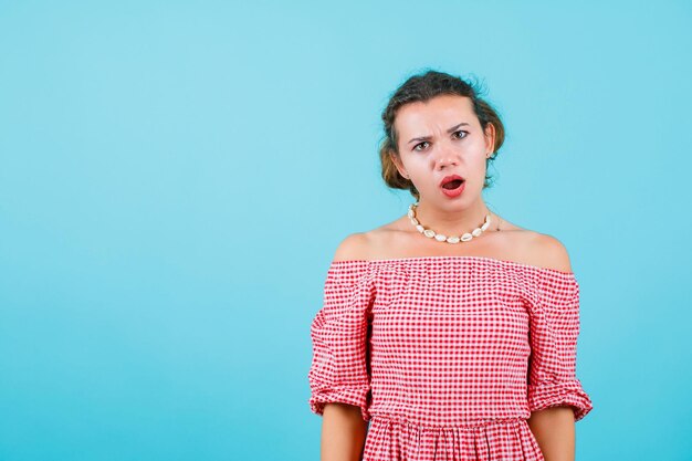 Surprised young girl is looking at camera by opening mouth on blue background