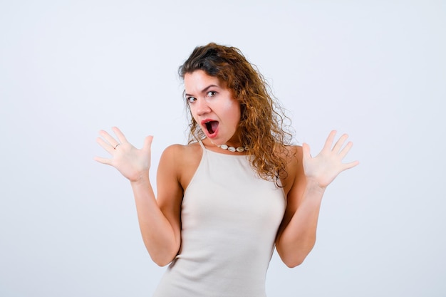 La ragazza sorpresa sta guardando la fotocamera aprendo le mani su sfondo bianco