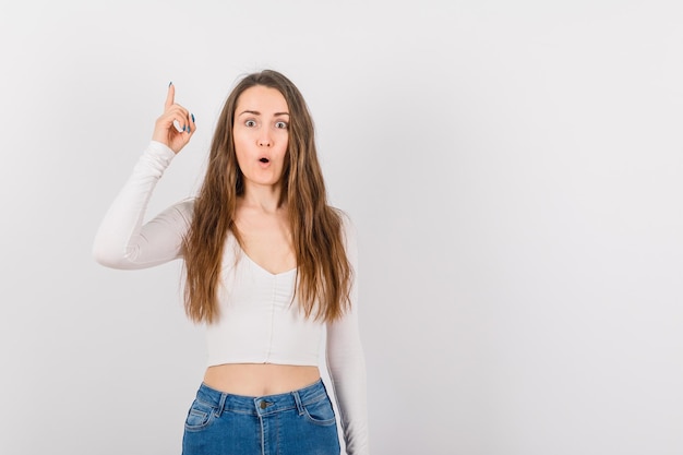 Surprised young girl is pointing up with forefinger on white background