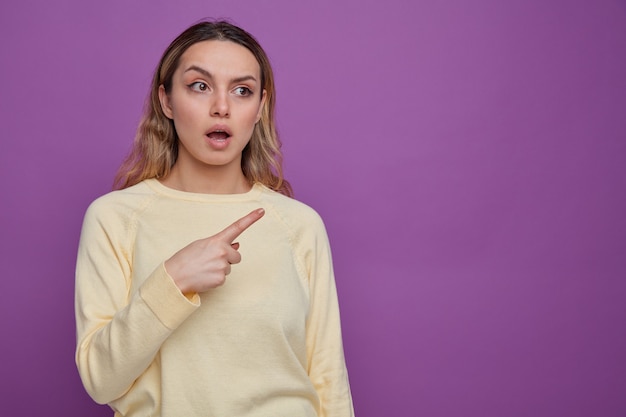 Free photo surprised young girl looking and pointing at side