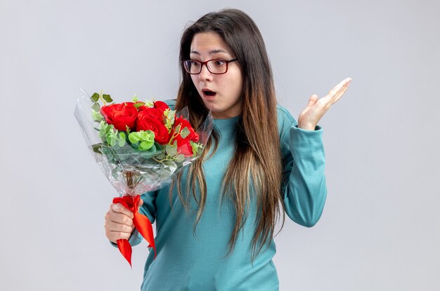 Surprised young girl on valentines day holding and looking at bouquet spreading hand isolated on white background