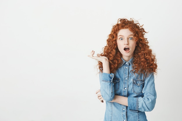 Surprised young girl with curly red hair with opened eyes . Copy space.