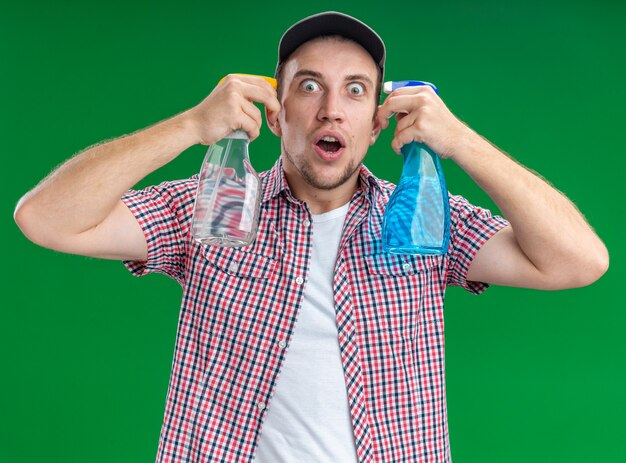 surprised young guy cleaner wearing cap showing suicide gesture with cleaning agent isolated on green wall