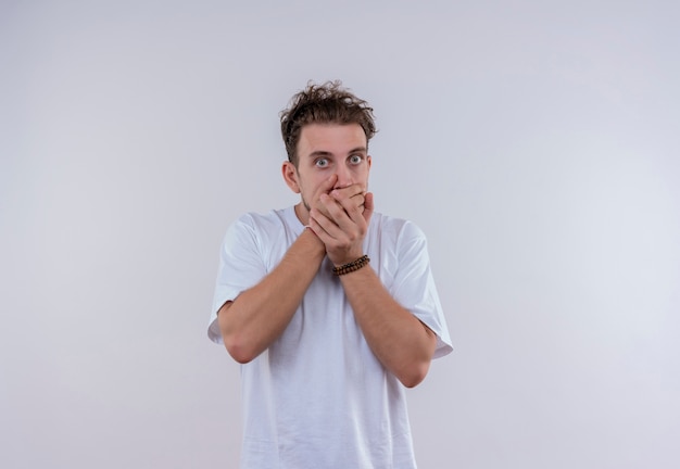 Surprised young guy wearing white t-shirt covered mouth with hands on isolated white background