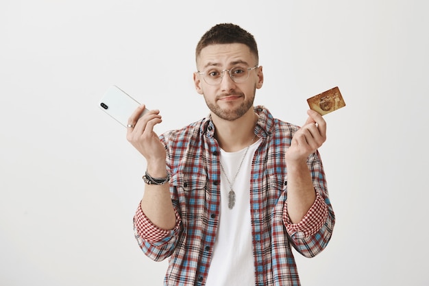 Surprised young guy with glasses posing with his phone  and card