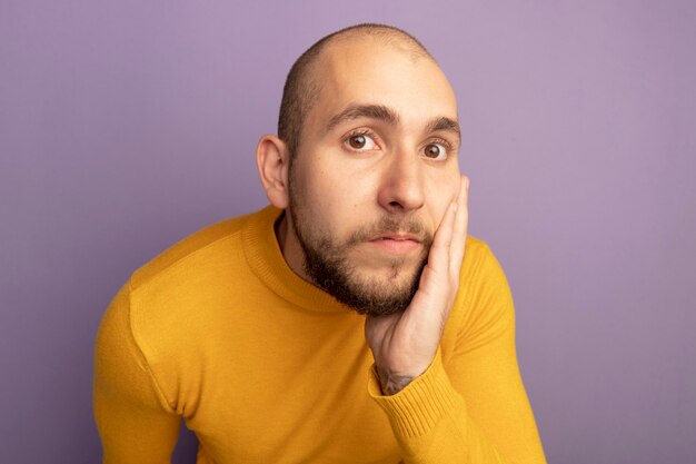 Surprised young handsome guy putting hand on cheek