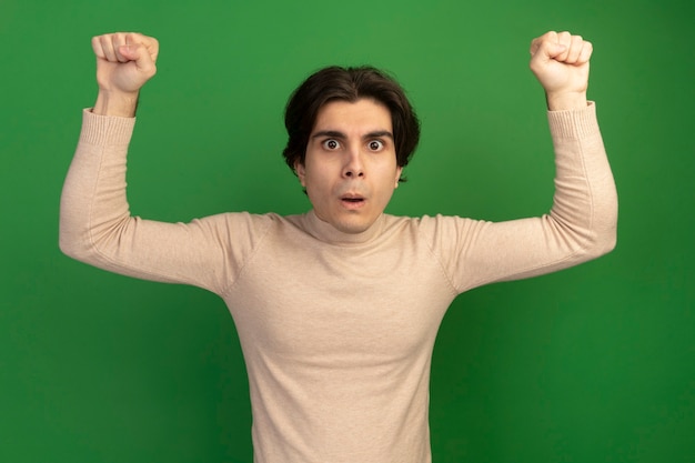Бесплатное фото Удивленный молодой красивый парень, поднимающий кулаки на зеленой стене