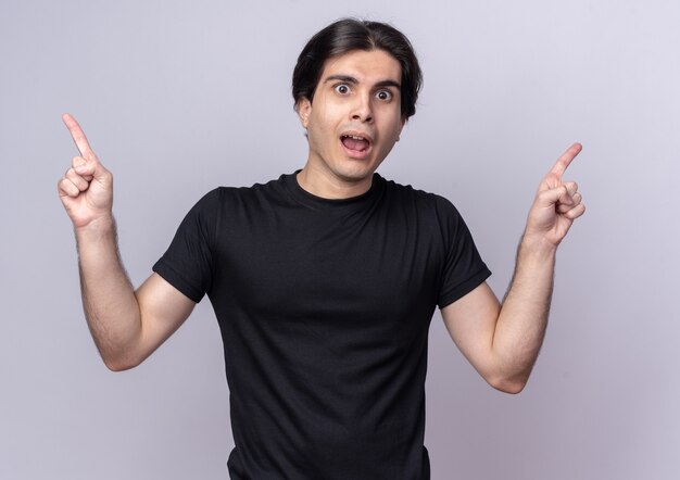 Surprised young handsome guy wearing black t-shirt points at differents sides isolated on white wall