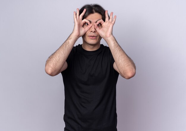 Surprised young handsome guy wearing black t-shirt showing look gesture isolated on white wall