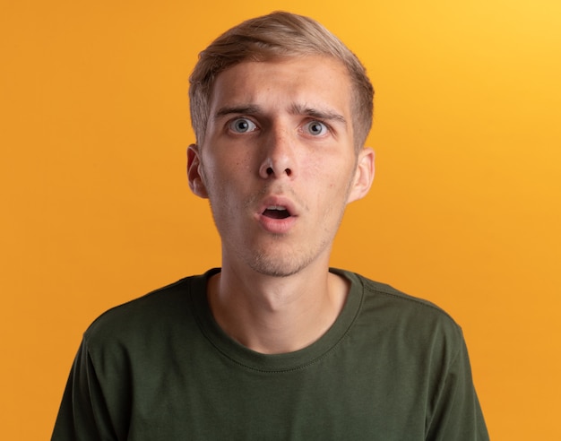 Surprised  young handsome guy wearing green shirt isolated on yellow wall