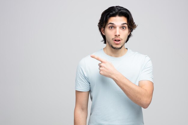 surprised young handsome man looking at camera pointing to side isolated on white background with copy space