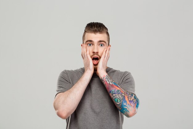 Surprised young handsome man posing over grey wall.