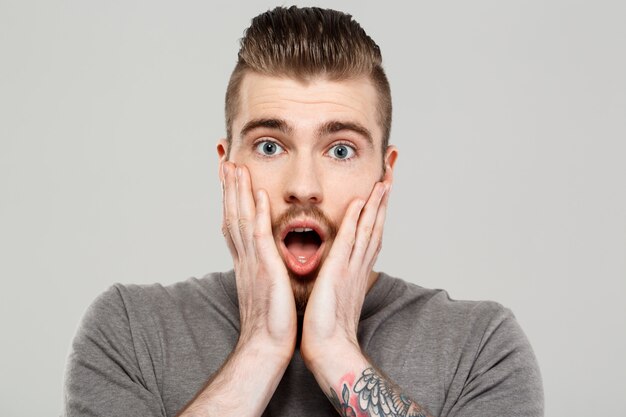 Surprised young handsome man posing over grey wall.