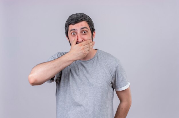 Surprised young handsome man putting hand on mouth isolated on white wall