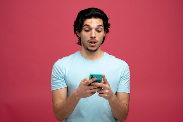 surprised young handsome man using his mobile phone isolated on red background