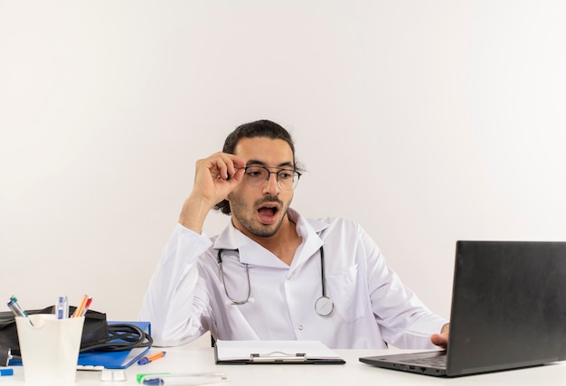 Удивленный молодой мужчина-врач в медицинских очках в медицинском халате со стетоскопом