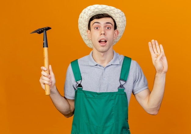 Free photo surprised young male gardener wearing gardening hat holds rake and gestures