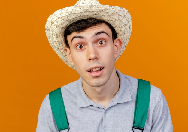 Surprised young male gardener wearing gardening hat looks at camera