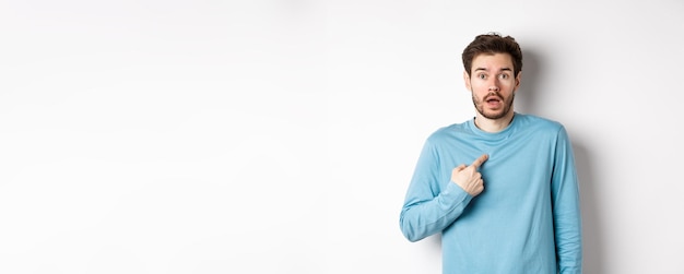 Free photo surprised young man gasping and pointing at himself with disbelief being chosen or named standing ov