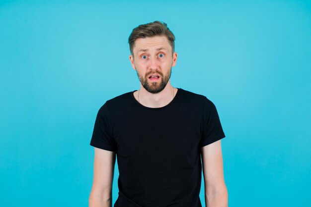 Surprised young man is looking at camera on blue background