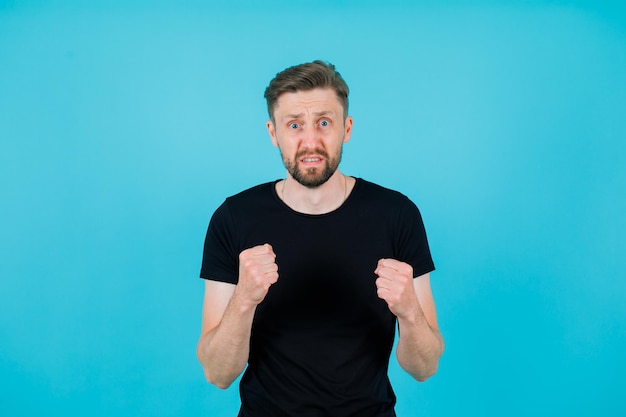 Surprised young man is raising up her fists on blue background
