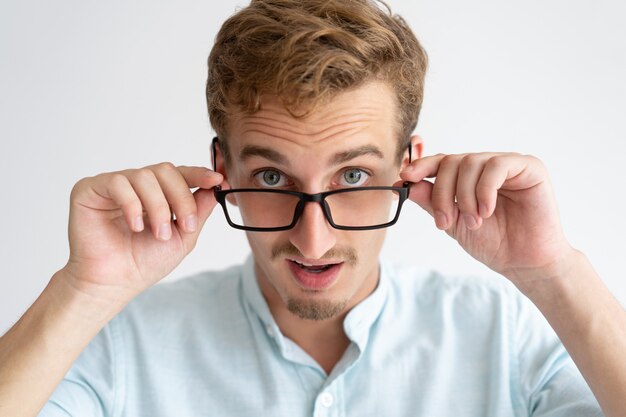Surprised young man looking at camera over glasses