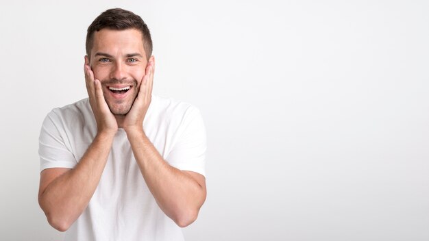 Surprised young man looking at camera standing against white wall