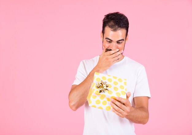 Surprised young man looking at open gift box against pink background