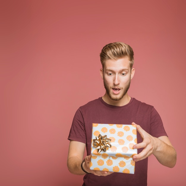 Surprised young man opening floral gift box with golden bow