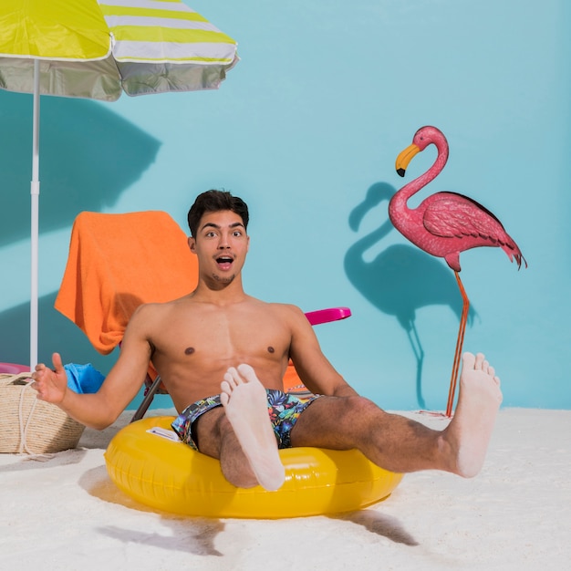 Surprised young man sitting on swimming circle in studio