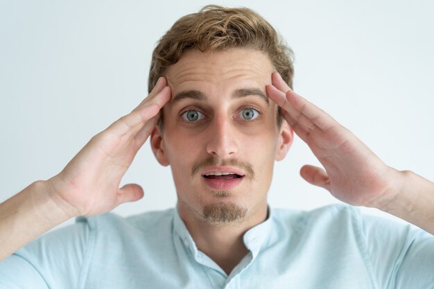 Surprised young man touching temples with his mouth open. 