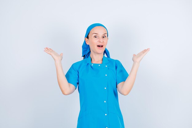 Удивленная молодая медсестра смотрит в камеру, широко раскрывая руки на белом фоне