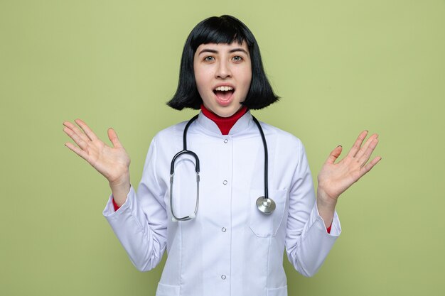 Удивленная молодая симпатичная кавказская девушка в униформе врача со стетоскопом, взявшись за руки