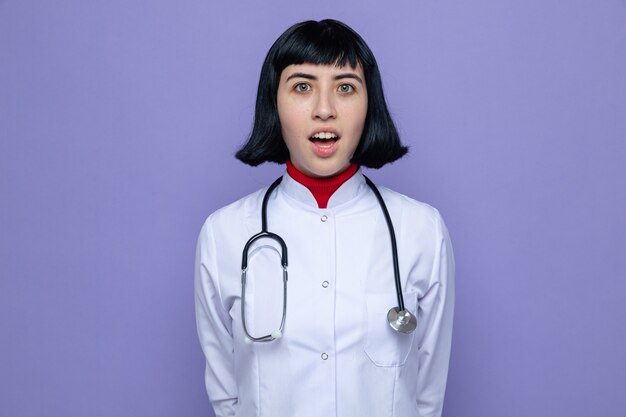 聴診器が立っている医者の制服を着た驚くべき若いかなり白人の女の子と