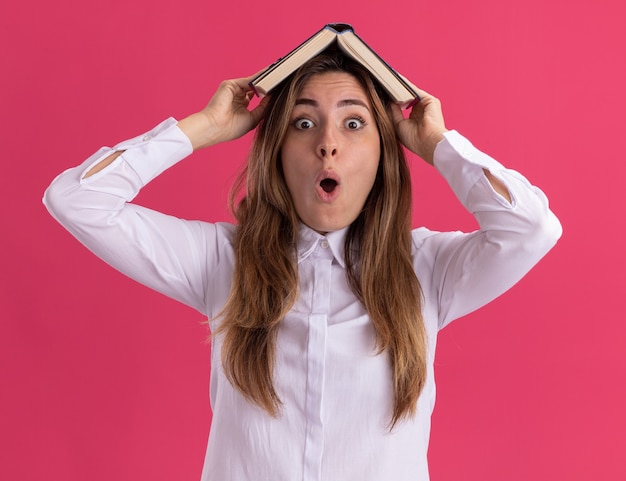 Surprised young pretty caucasian girl holds book over head